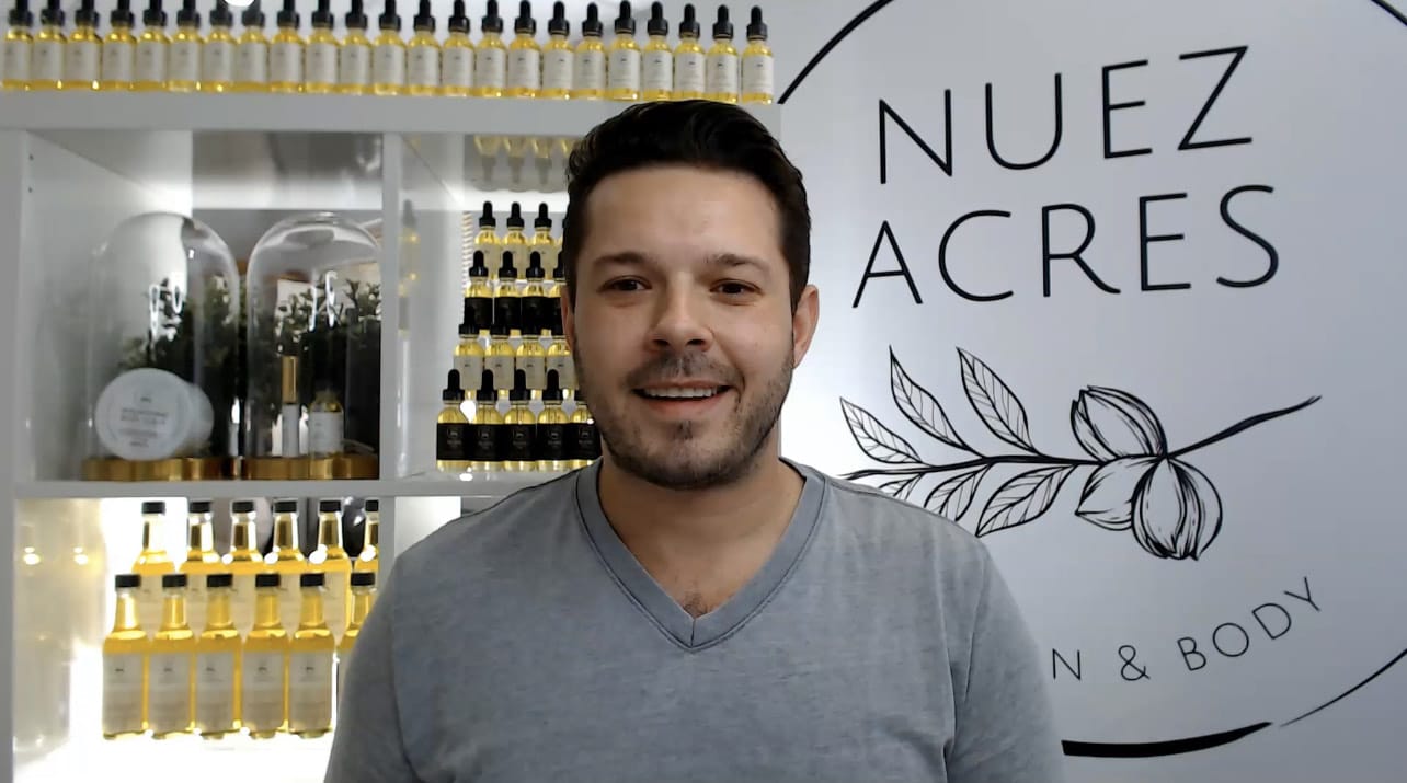 Anthony Wingham smiles at the camera, with a Nuez Acres sign and product bottles in the background.
