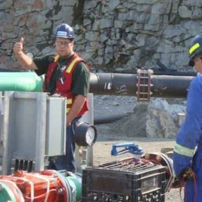 Matthew Oillette stands at a work site, wearing a high visibility vest. There is equipment in the foreground. 