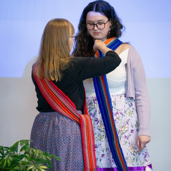 A woman places a sash on a youth at an award ceremony.