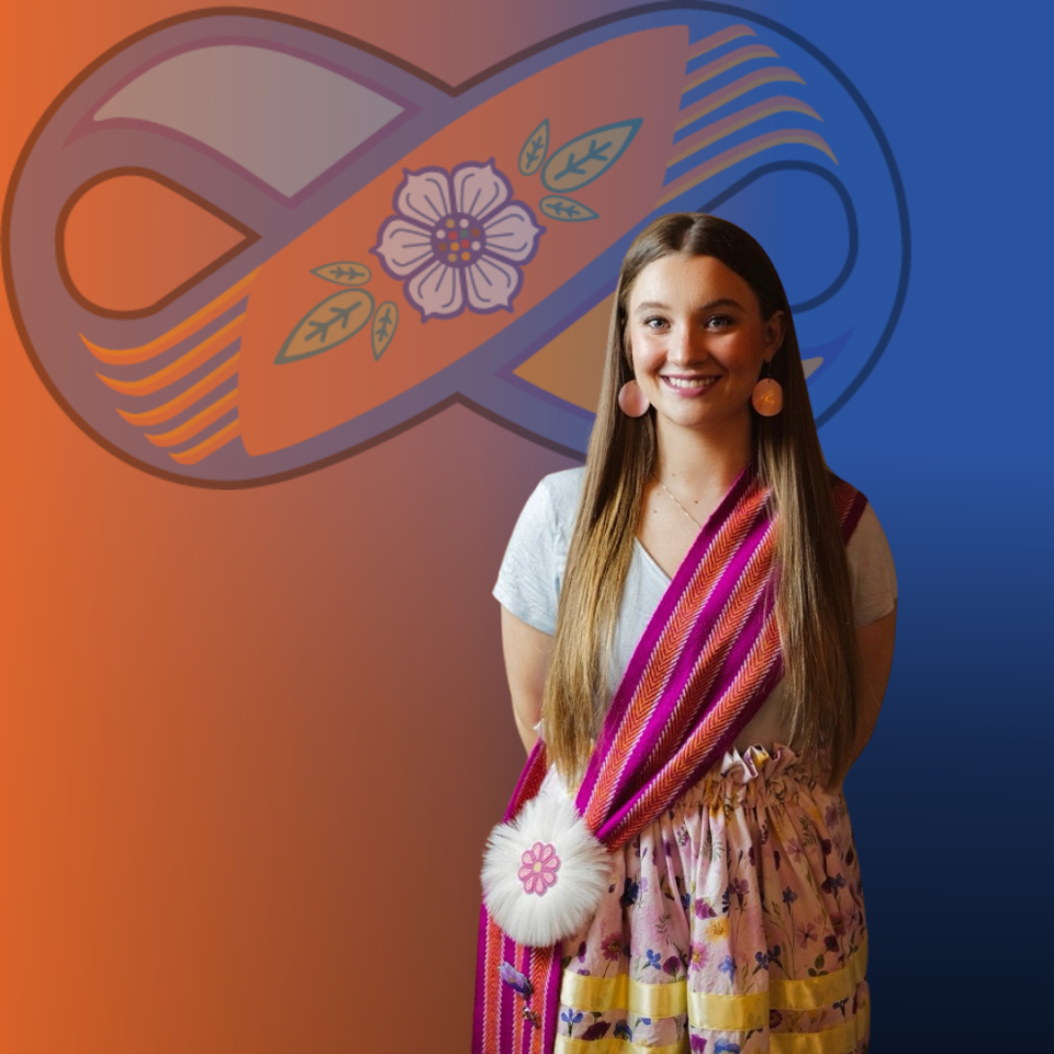 She has long brown hair that’s parted in the middle, it falls straight down past her shoulders. She has a warm smile, with her eyes slightly squinting which adds to her cheerful expression. Her eyes are blue and and her makeup is subtle, with a hint of pink lipstick that complements her earrings. She has large circular pink conch shell earrings on. Her skin tone is fair, the lighting highlights one side of her face more than the other. There is a delicate chain necklace around her neck.