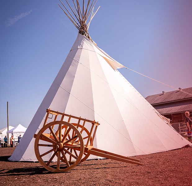 A large white Tipi with a wooden Métis wheelbarrow in front of it.