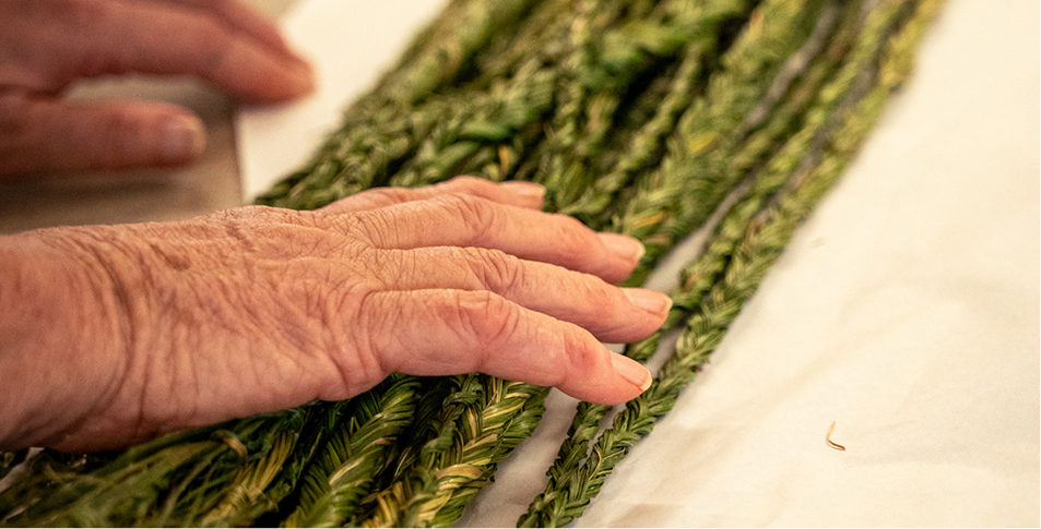 A close-up of hands preparing sweet grass.