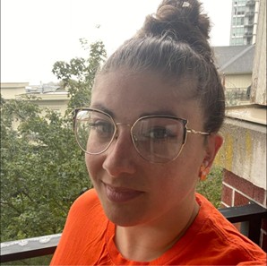 Katy Carson is smiling in an orange shirt against an outdoor background.
