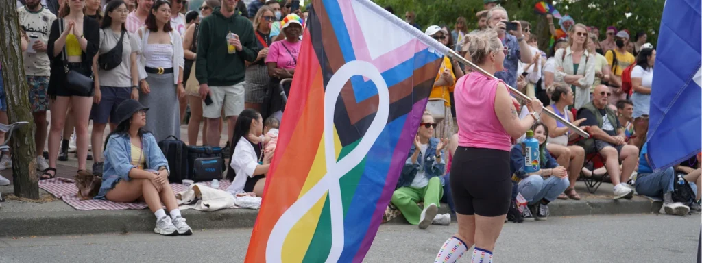 A woman carrying the Métis Pride flag in front of a crowd of people watching the Pride parade.