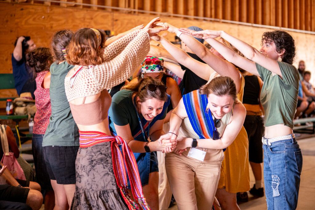 Two women walk under a tunnel of people with their arms raised for an indoor cultural activity.