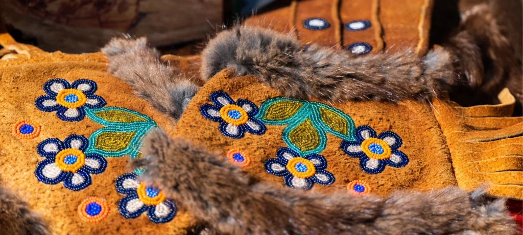 Traditional Métis gloves with embroidered colourful beaded flowers on them and a furry belt wrapped around.
