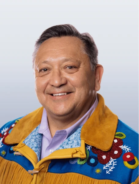 Dean Gladue is smiling in a tan-coloured jacket with Métis beading against a white background.