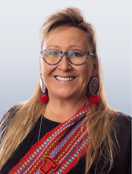 Melanie Allard is smiling, wearing a red Métis sash with an Orange Shirt Day pin against a neutral background.