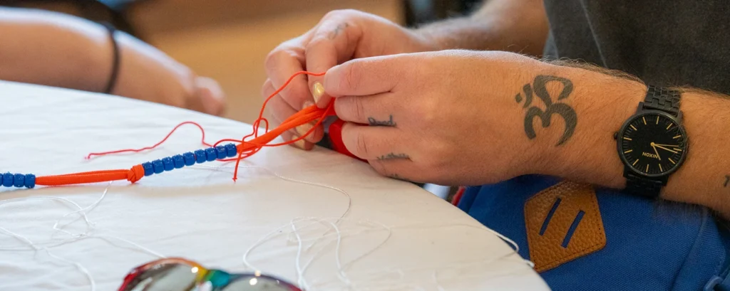 A person's hands working on a beaded craft activity at a table.